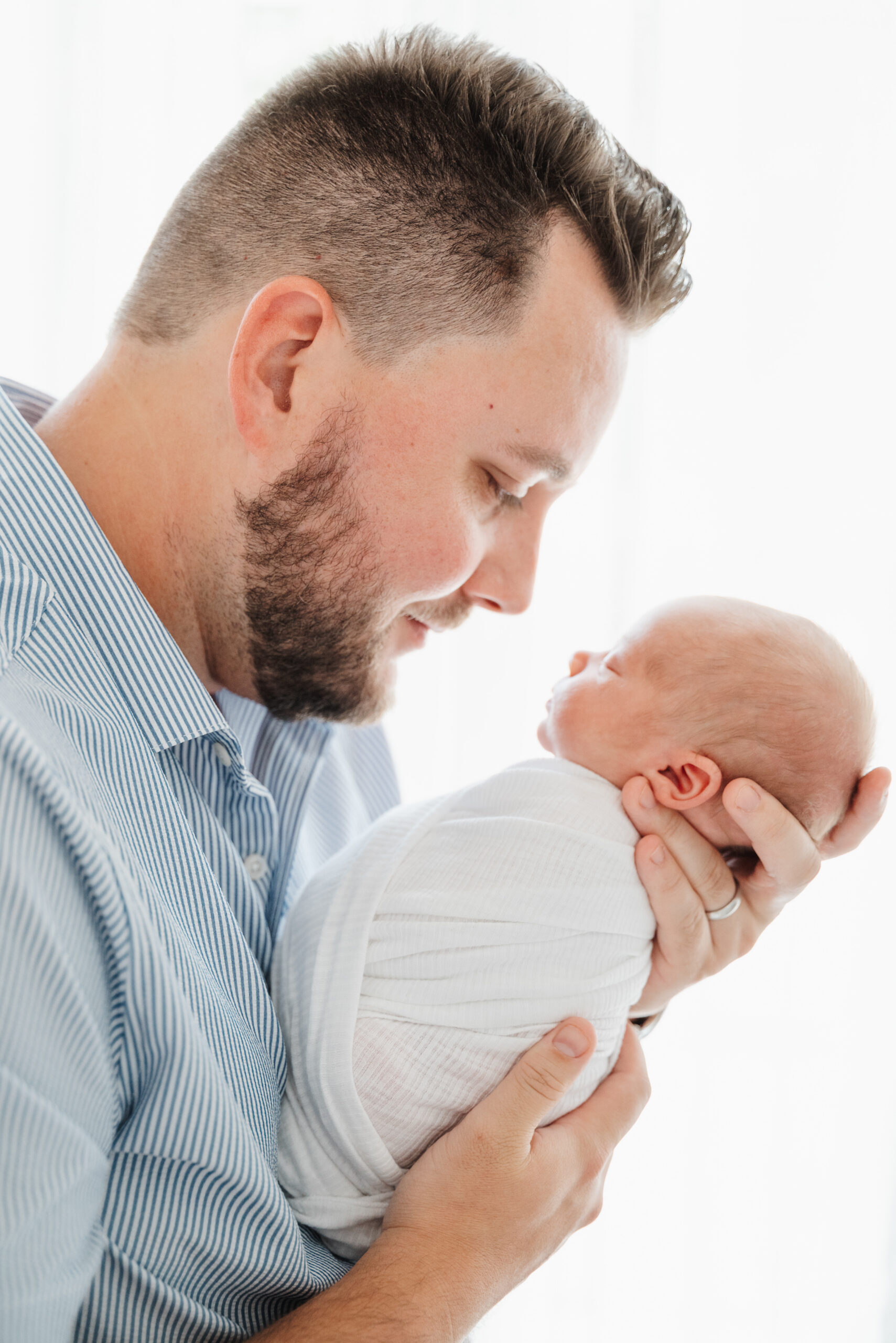 Dad cradles baby boy and looks into his eyes in Cumming newborn session.
