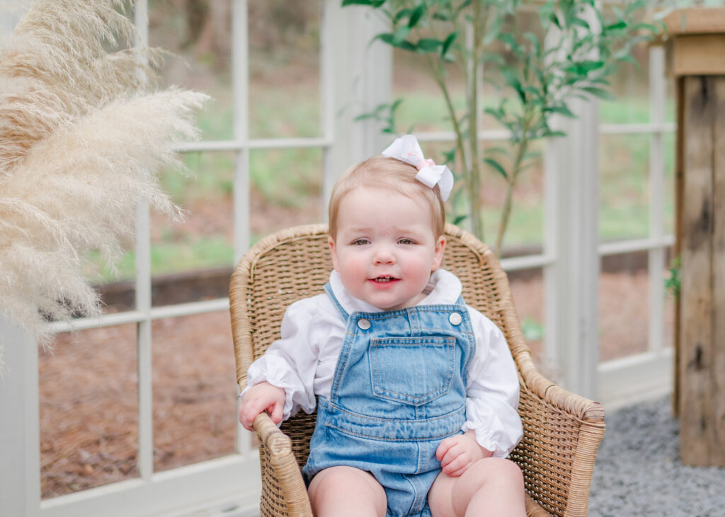 Toddler girl sits in wicker chair during Easter event in Cumming, GA.