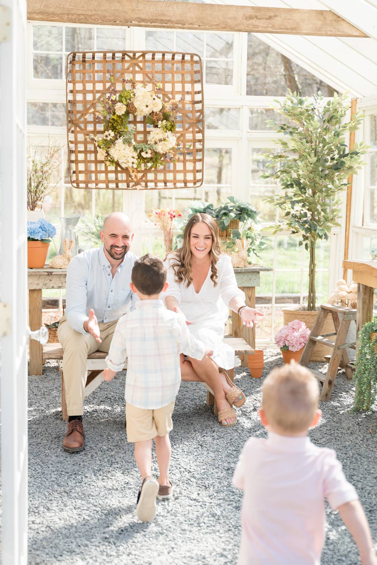 Toddler brothers run towards mom and dad sitting on a bench in a greenhouse