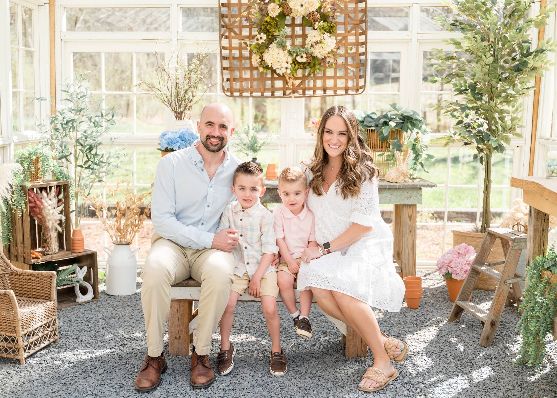 Happy mom and dad sit on a bench in a greenhouse with their two toddler sons before visiting alpharetta playgrounds