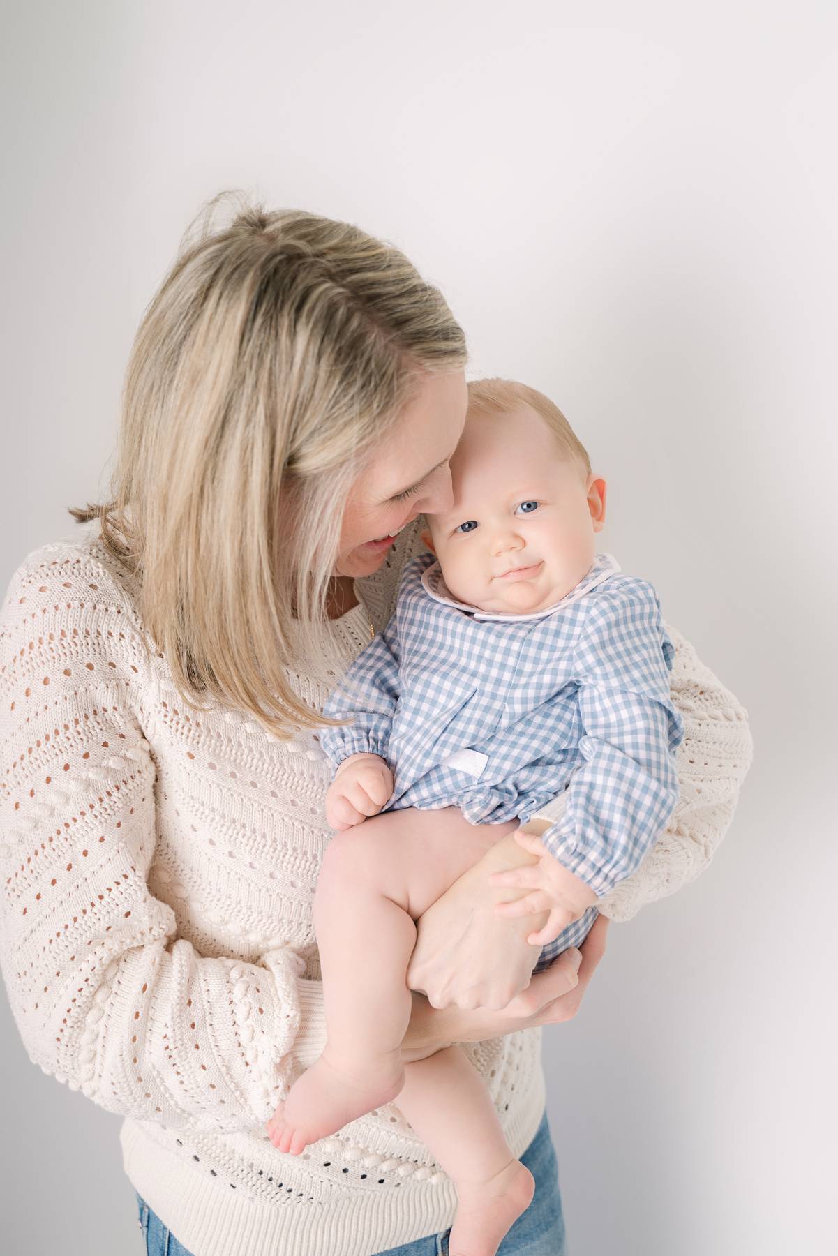 An infant in a blue onesie smiles in mom's arms after visiting baby boutiques in atlanta
