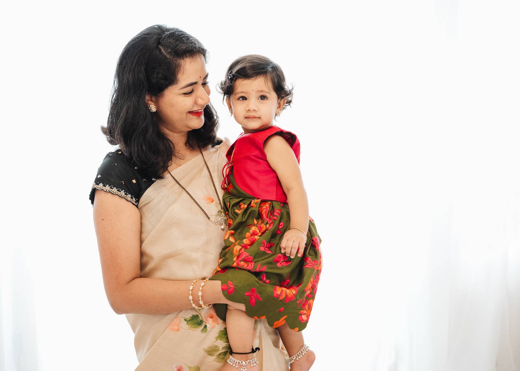 A happy mom holds her toddler daughter while standing in a window