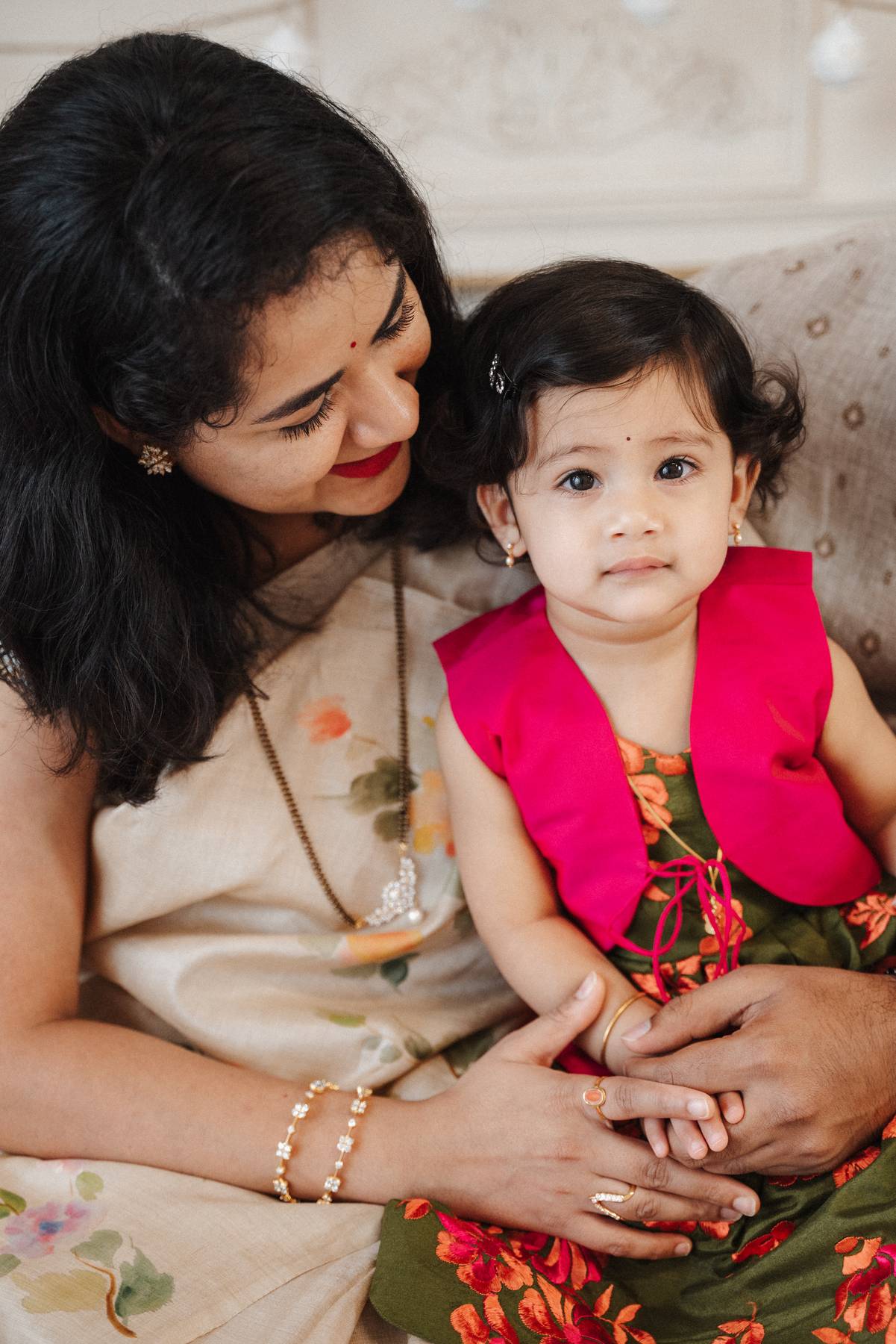 A toddler girl in a colorful dress sits in mom's lap on a couch before visiting family friendly restaurants in atlanta