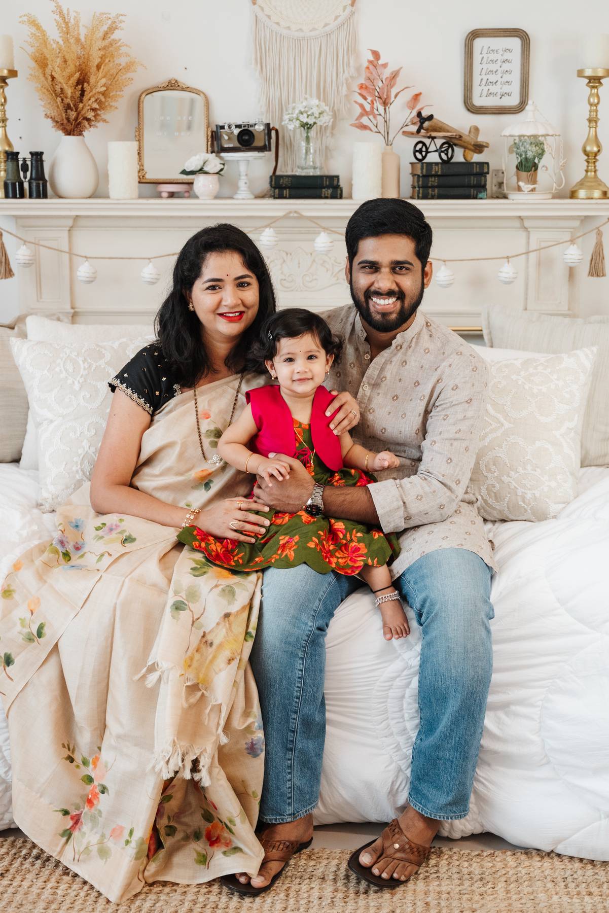 Smiling mom and dad sit on a daybed with their toddler daughter in a colorful dress in their laps before visiting family friendly restaurants in atlanta
