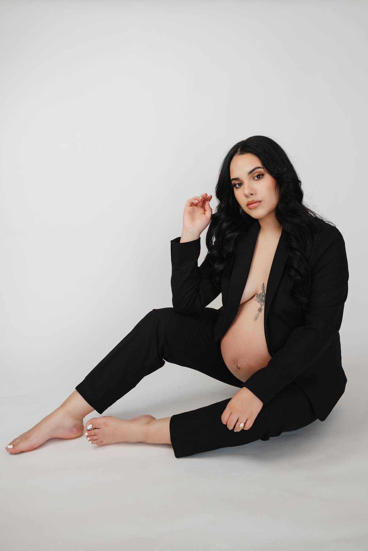 A pregnant woman sits on a studio floor in black pants and open blazer after visiting peachtree womens clinic