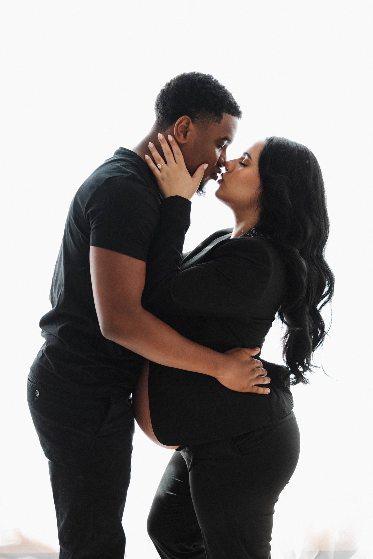 An expecting couple lean in for a kiss in a studio window wearing black after visiting peachtree womens clinic