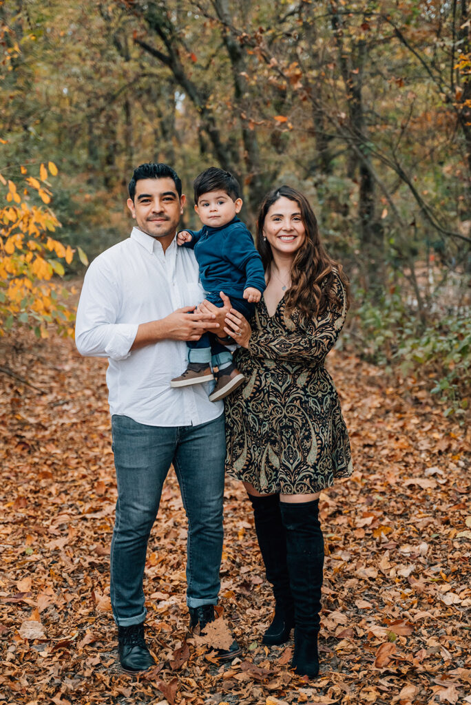 Family of three smiling together outdoors during Cumming GA fall family portraits.