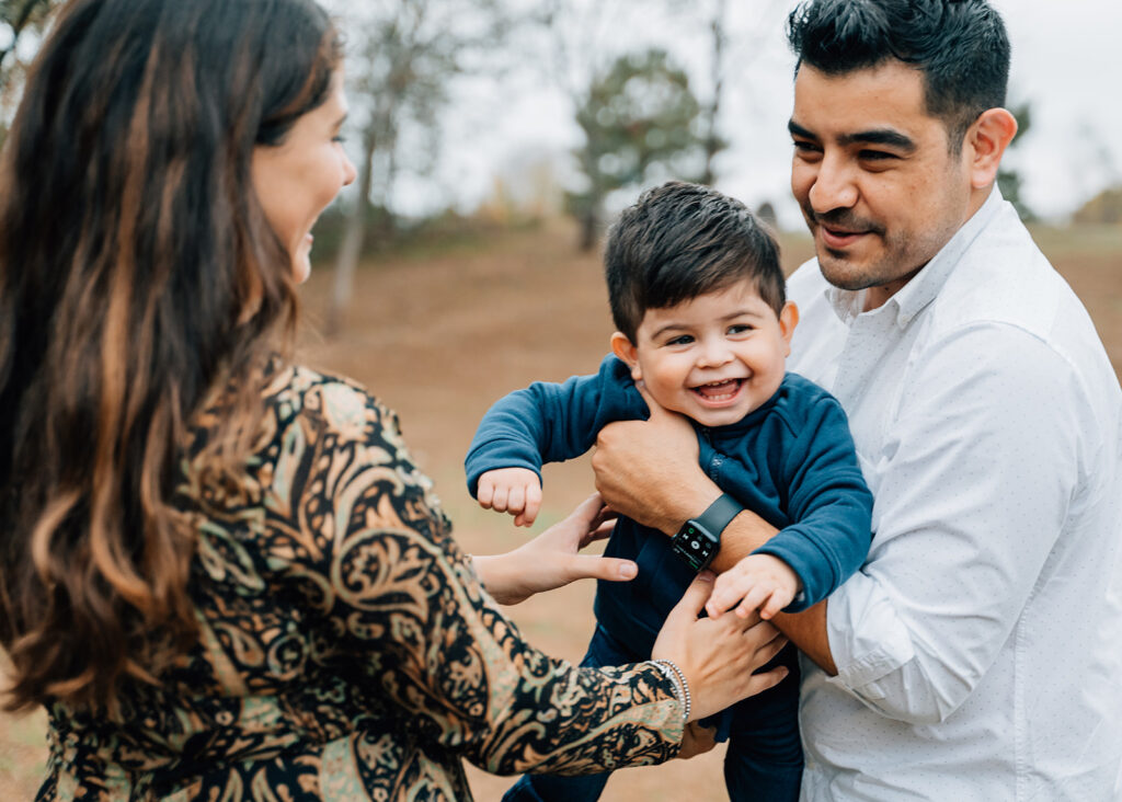Parents laughing while holding young child during fall family session in North Atlanta