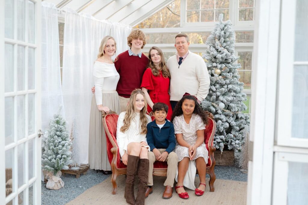 Large family posing for picture in Christmas themed greenhouse while showing off their coordinating Christmas outfits for family photos.