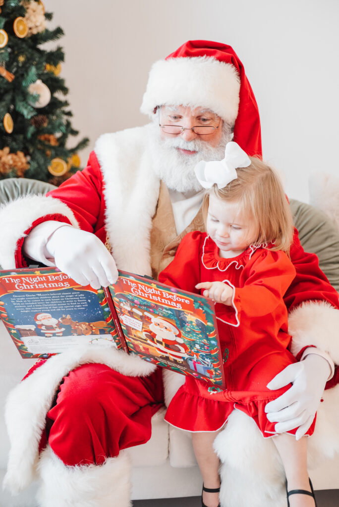 Santa in red suit reads to little girl in red nightgown.