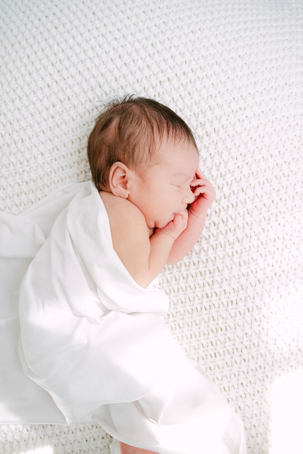 Baby sleeping while loosely wrapped in white blanket.
