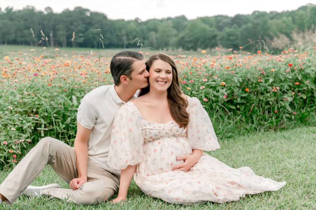 Husband and wife sit together while husband kisses wife's cheek in a flower field at Prospect Farms.