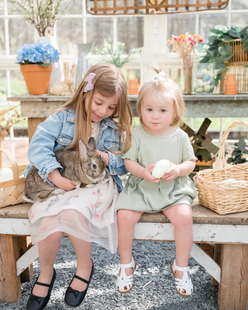 Two young girls sit on a bench holding a brown bunny in Atlanta Easter photography Session. 