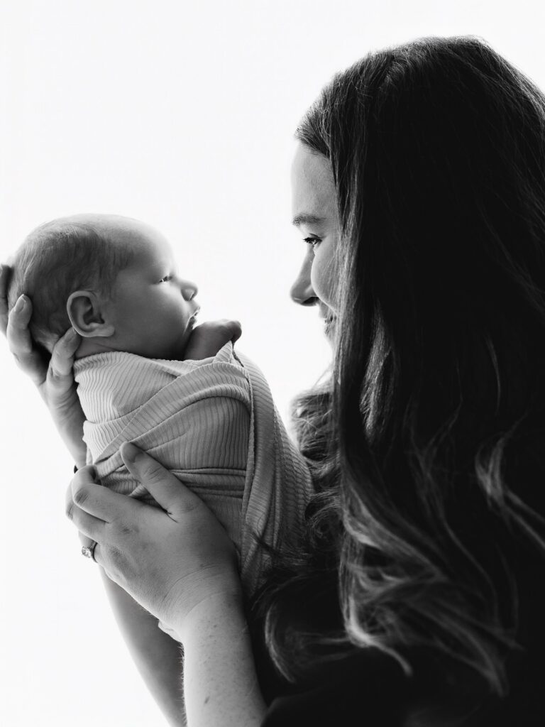 Mom looking into her newborn son's eyes while holding him in black and white studio newborn image.