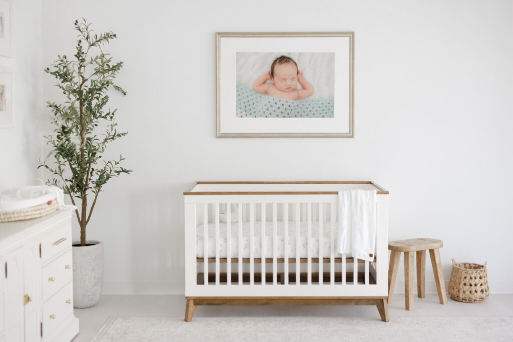 White, minimalist nursery with framed image of baby sleeping with a blue blanket.