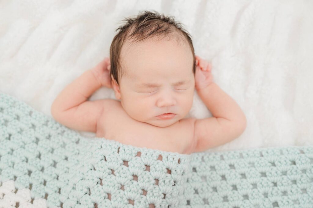 Baby boy sleeping with a blue blanket placed across him.