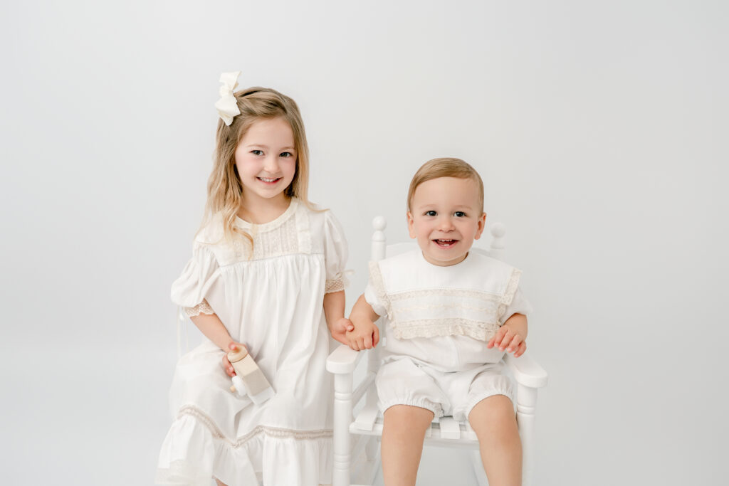 Brother and sister sitting together during an Atlanta heirloom portrait session, dressed in classic light-toned outfits