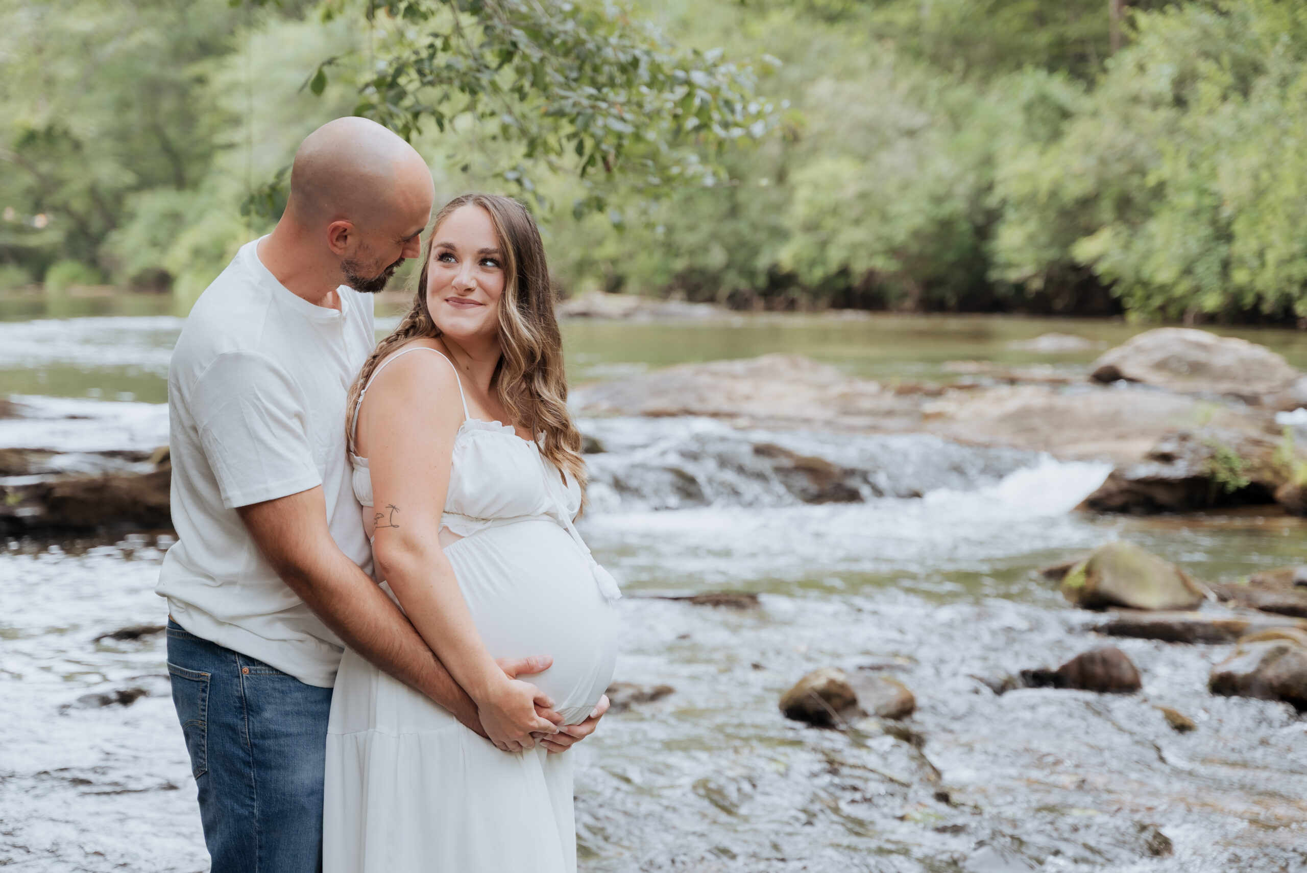 Mom and dad look into eachother's eyes while standing in river during Maternity photoshoot.