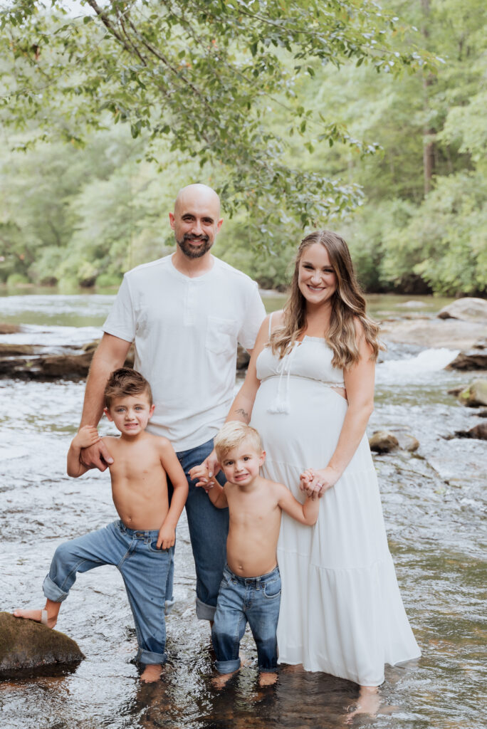Family poses together while stanfing on rocks in river.