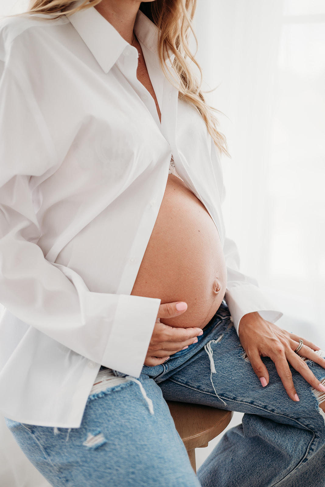 Pregnant mom wearing white button down shirt places hand on belly