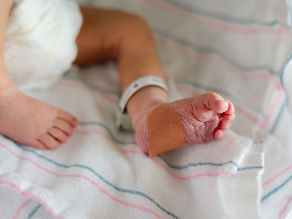 Image of a newborn's foot in hospital bassinet with hospital bracelet on ankle.