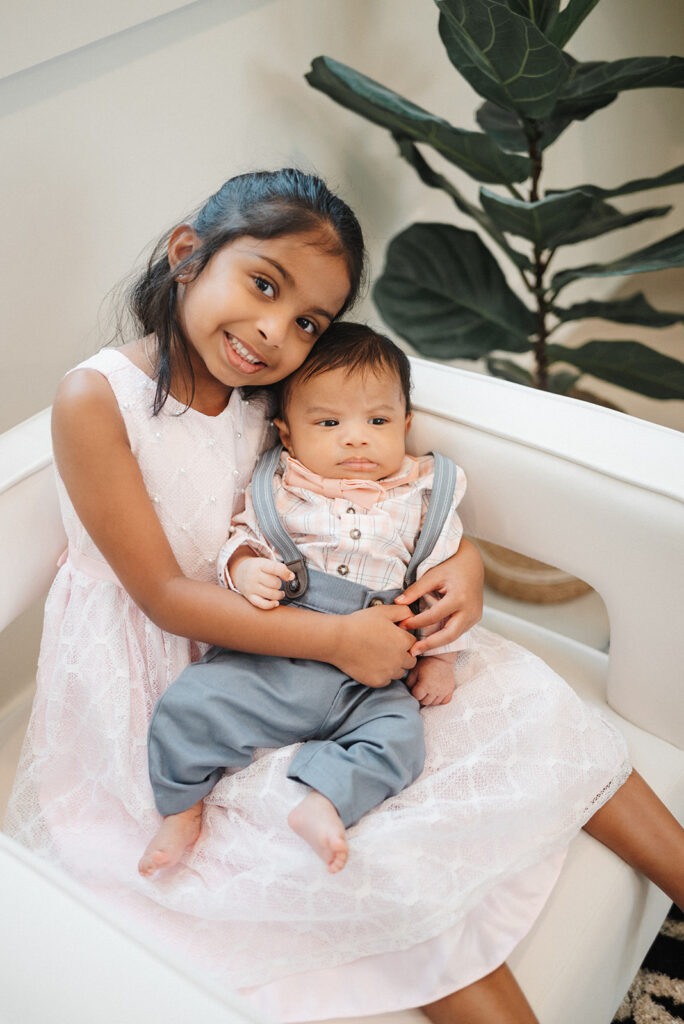 Girl in pink dress holds baby brother in Atlanta Newborn Photography Session.